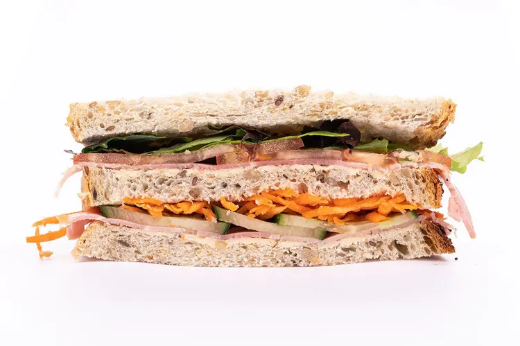 Sandwich club Dagobert en coupe — trois tranches de pain aux graines garnies de jambon, fromage, carottes râpées, concombre et salade