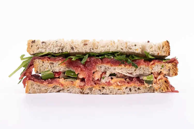 Sandwich La Complètement Marteau sur pain aux graines — carpaccio de bœuf rouge en gros plan, garniture crémeuse et roquette