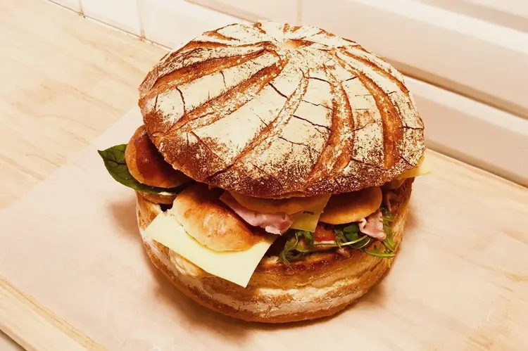 Pain surprise rond rustique avec couvercle de pain de campagne fariné, garni de mini-sandwiches au jambon-fromage visibles sur le côté, posé sur planche en bois