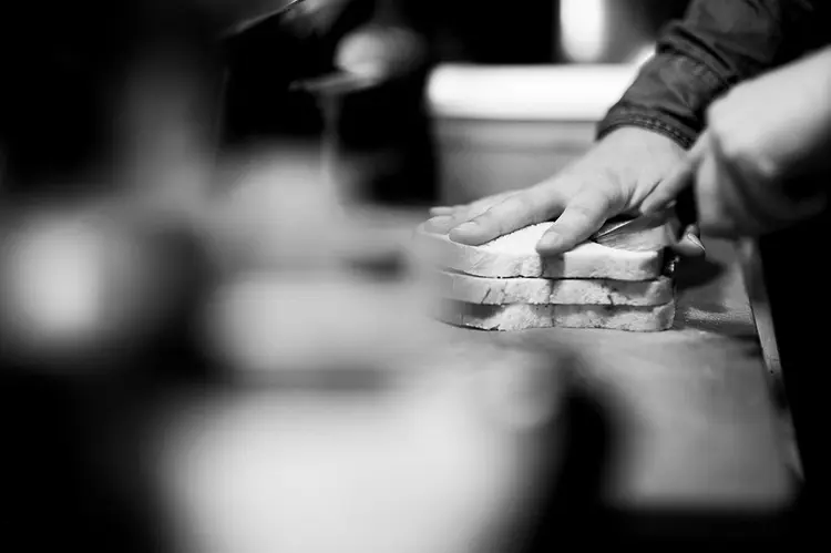 Mains préparant des tranches de pain de mie dans l'atelier de la sandwicherie Tartineke à Wavre, photo noir et blanc