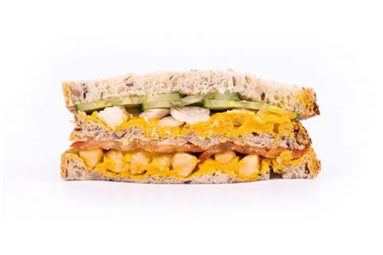 Sandwich vegan Le Moumouss en coupe — houmous de lentilles corail jaune doré, pois chiches et lamelles de concombre sur pain aux graines